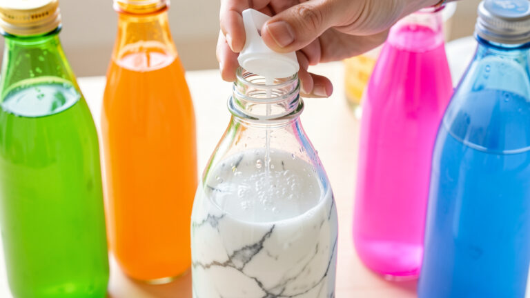 Bouteille de soda japonais à bille en verre ouverte avec son poussoir, entourée de plusieurs bouteilles colorées aux saveurs variées.